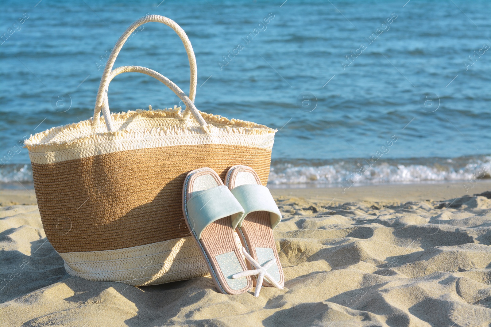 Photo of Straw bag, slippers and dry starfish on sandy beach near sea, space for text