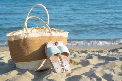 Photo of Straw bag, slippers and dry starfish on sandy beach near sea, space for text