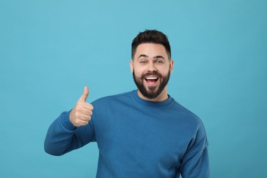 Photo of Happy young man with mustache showing thumb up on light blue background