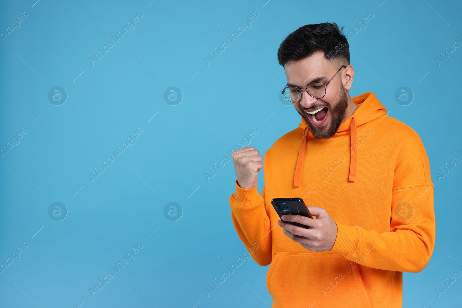 Photo of Happy young man using smartphone on light blue background, space for text