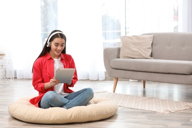 Photo of Young woman with headphones and tablet sitting on floor in living room