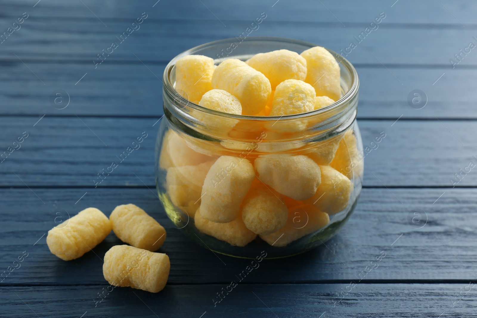 Photo of Jar of delicious crispy corn sticks on blue wooden table