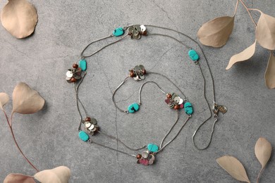 Beautiful necklace with gemstones and dried leaves on grey background, flat lay