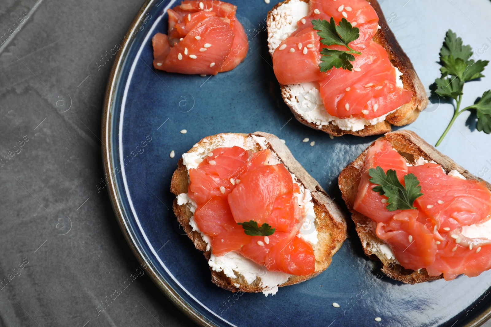 Photo of Tasty bruschettas with salmon, cream cheese and parsley on grey table, top view