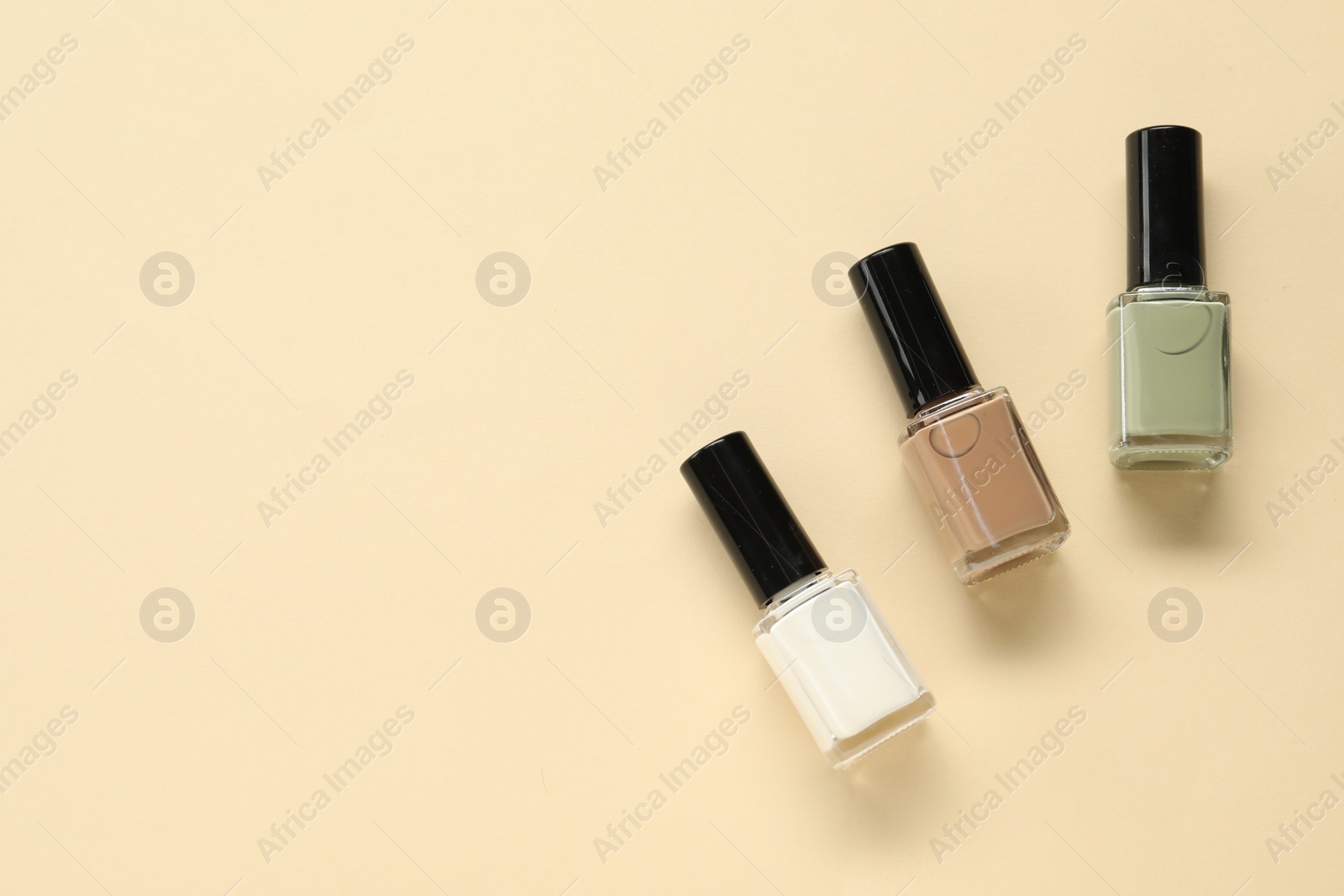 Photo of Colorful nail polishes in bottles on beige background, flat lay. Space for text