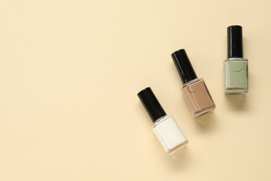 Colorful nail polishes in bottles on beige background, flat lay. Space for text