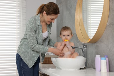 Mother washing her little baby in sink at home