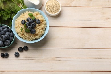 Photo of Tasty quinoa porridge with blueberries and mint in bowl on light wooden table, flat lay. Space for text