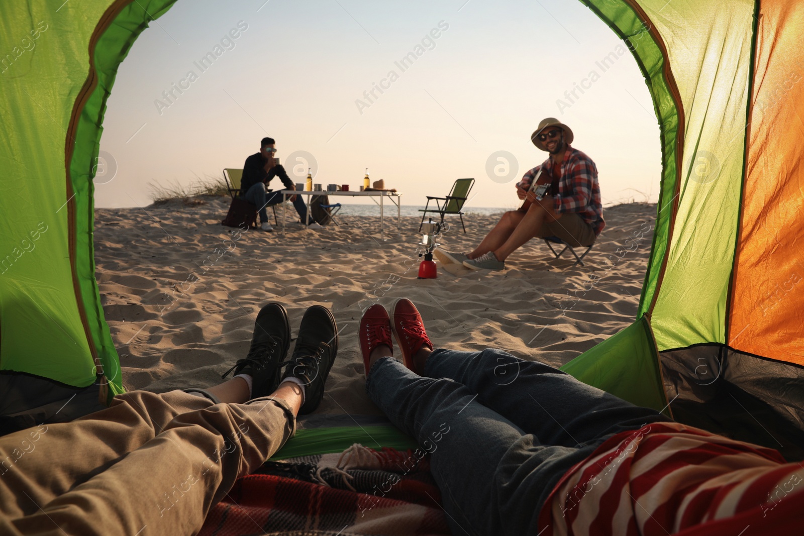 Photo of Friends resting on sandy beach, closeup. View from camping tent