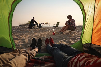 Friends resting on sandy beach, closeup. View from camping tent