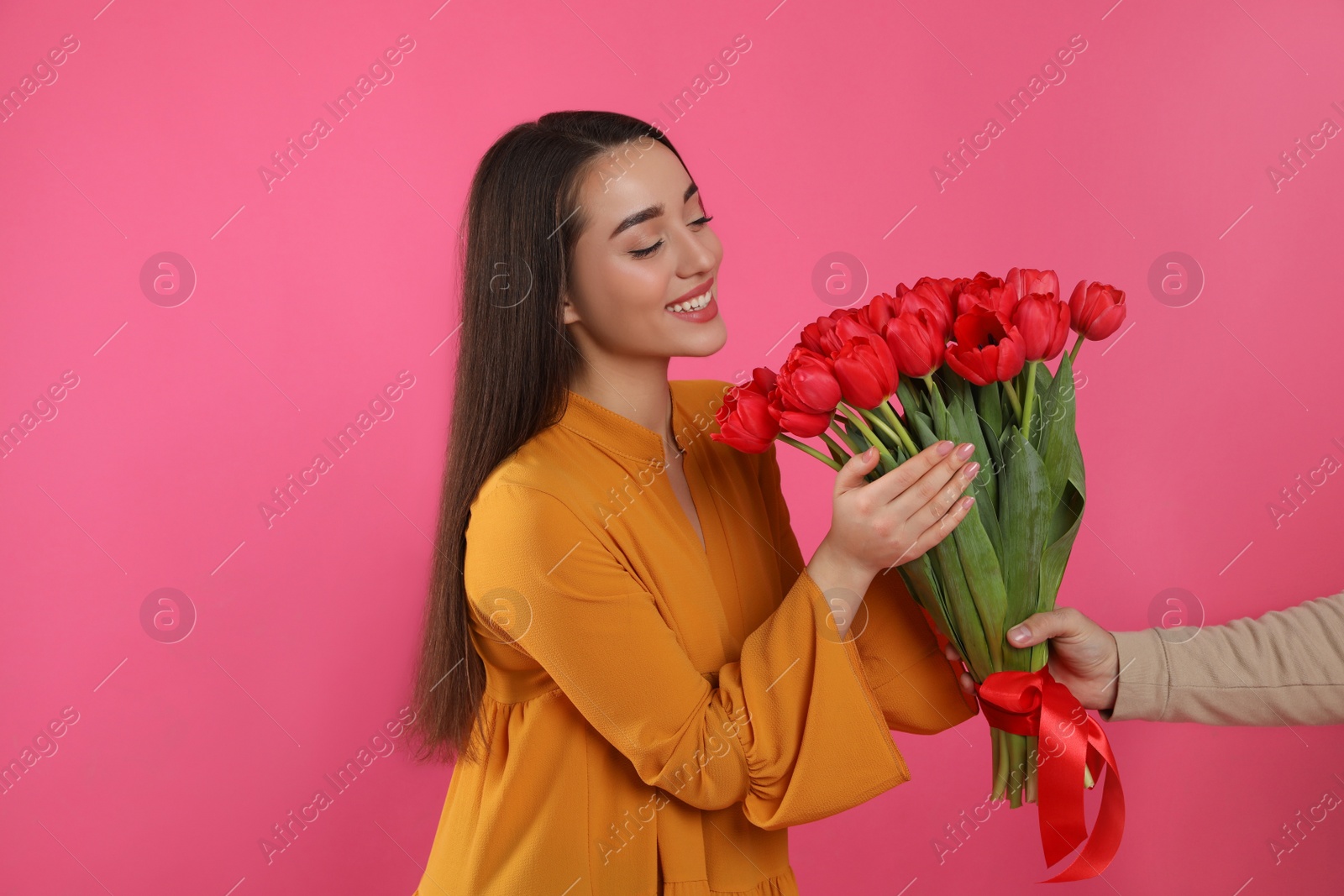 Photo of Happy woman receiving red tulip bouquet from man on pink background. 8th of March celebration