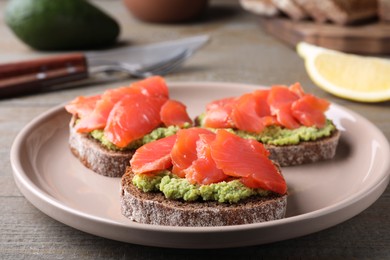 Delicious sandwiches with salmon and avocado on grey wooden table, closeup