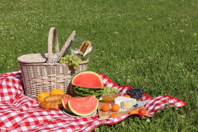 Photo of Picnic blanket with delicious food and wine outdoors on summer day, space for text