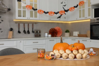 Photo of Kitchen decorated for Halloween. Pumpkins, candies and bunch of garlic on wooden table