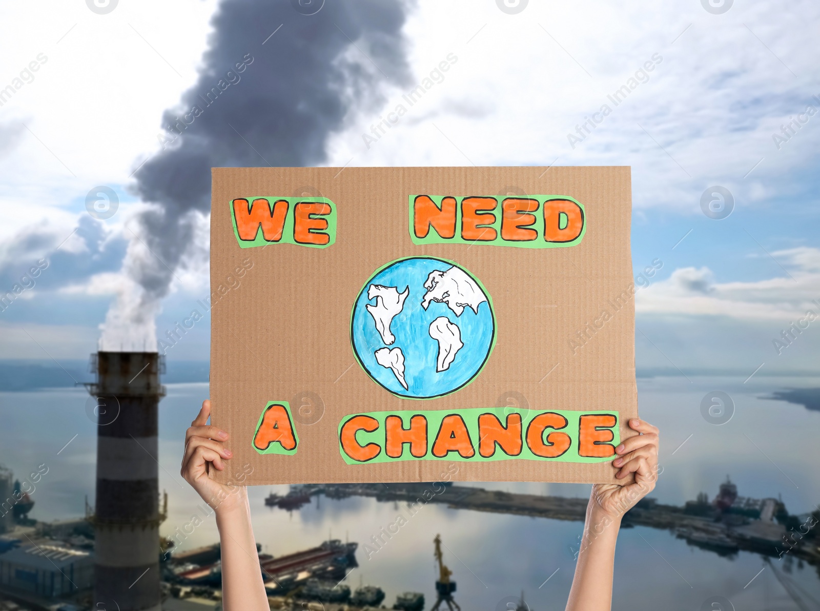 Image of Protestor holding placard with text We Need A Change and blurred view of industrial factory on background. Climate strike