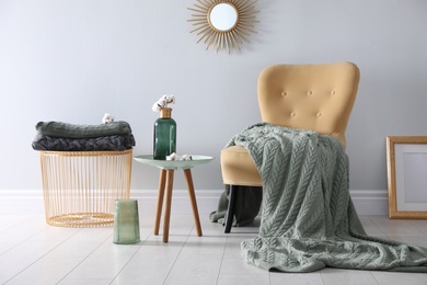 Photo of Soft knitted blanket on armchair in room. Home interior