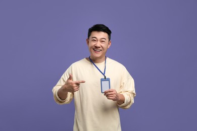 Photo of Happy asian man pointing at vip pass badge on purple background