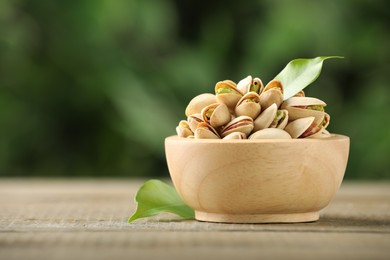 Tasty pistachios in bowl on wooden table against blurred background, closeup. Space for text