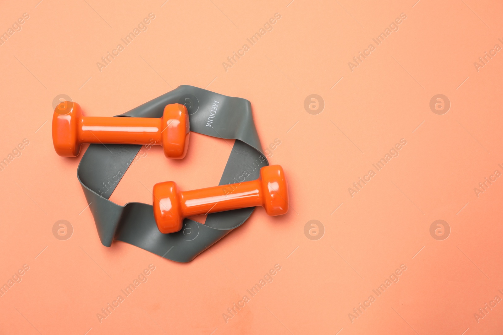 Photo of Dumbbells and fitness elastic band on coral background, flat lay. Space for text