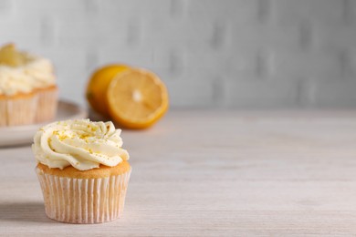 Delicious cupcake with white cream and lemon zest on light wooden table, space for text