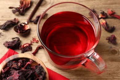 Photo of Cup of fresh hibiscus tea and dry flower leaves on wooden table, closeup