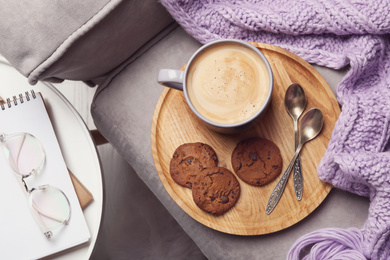 Photo of Cup of hot coffee and cookies on armchair, top view. Winter drink