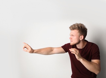 Young man outstretching hand on light background. Vision problem