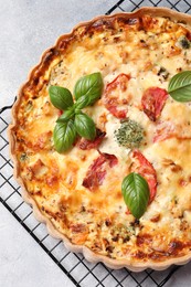 Photo of Tasty quiche with tomatoes, basil and cheese on light textured table, top view