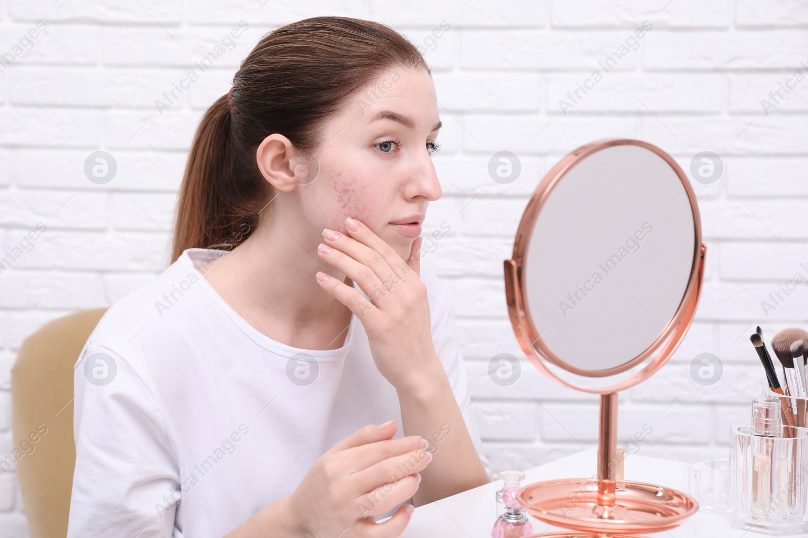 Photo of Woman with acne problem looking at mirror indoors