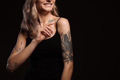 Photo of Beautiful woman with tattoos on body against black background, closeup. Space for text