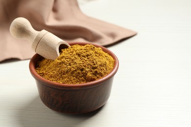 Photo of Curry powder in bowl and scoop on white wooden table, space for text