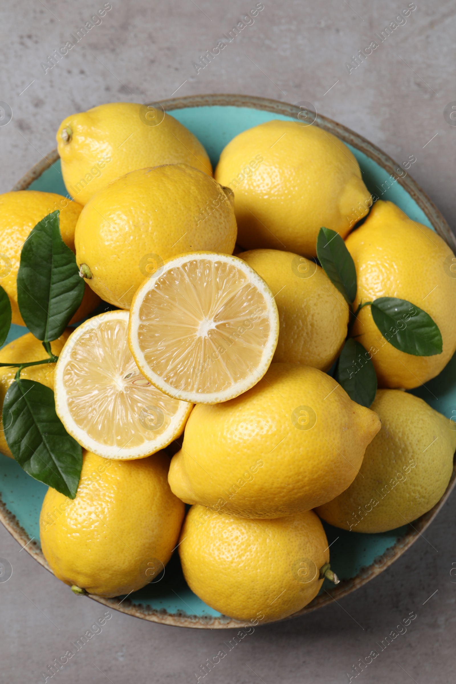 Photo of Fresh lemons and green leaves on grey table, top view