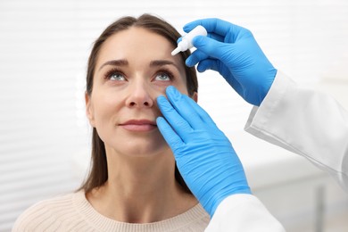 Photo of Doctor applying medical drops into woman's eye indoors