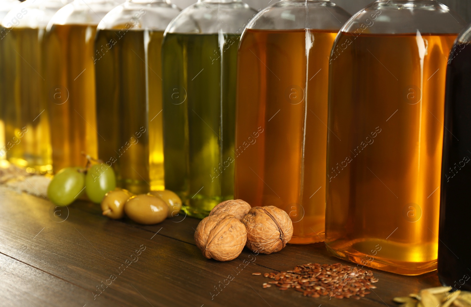 Photo of Vegetable fats. Different oils in glass bottles and ingredients on wooden table, closeup