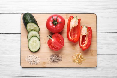 Fresh cucumbers, red bell peppers, tomatoes and vegetable seeds on white wooden table, top view