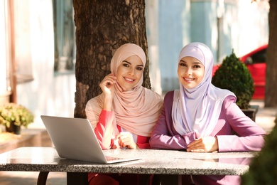 Muslim women with laptop sitting in outdoor cafe