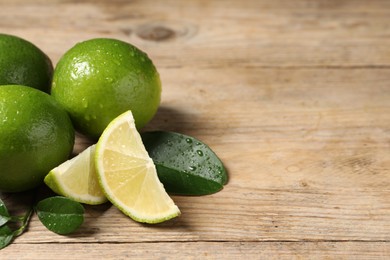 Photo of Fresh limes and green leaves with water drops on wooden table