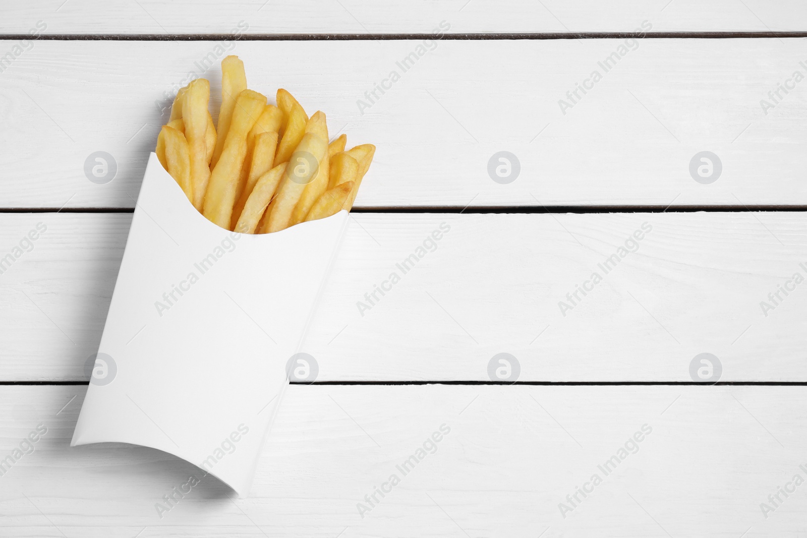 Photo of Delicious french fries in paper box on white wooden table, top view. Space for text