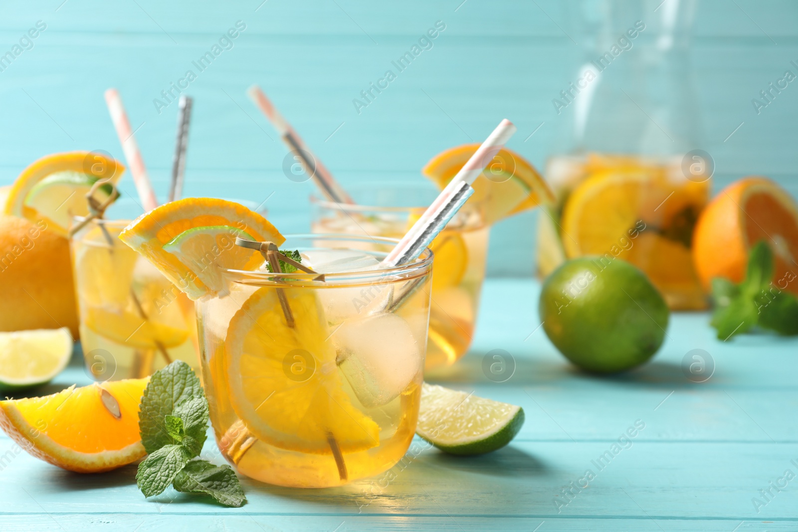 Photo of Delicious refreshing drink with orange and lime slices on light blue wooden table