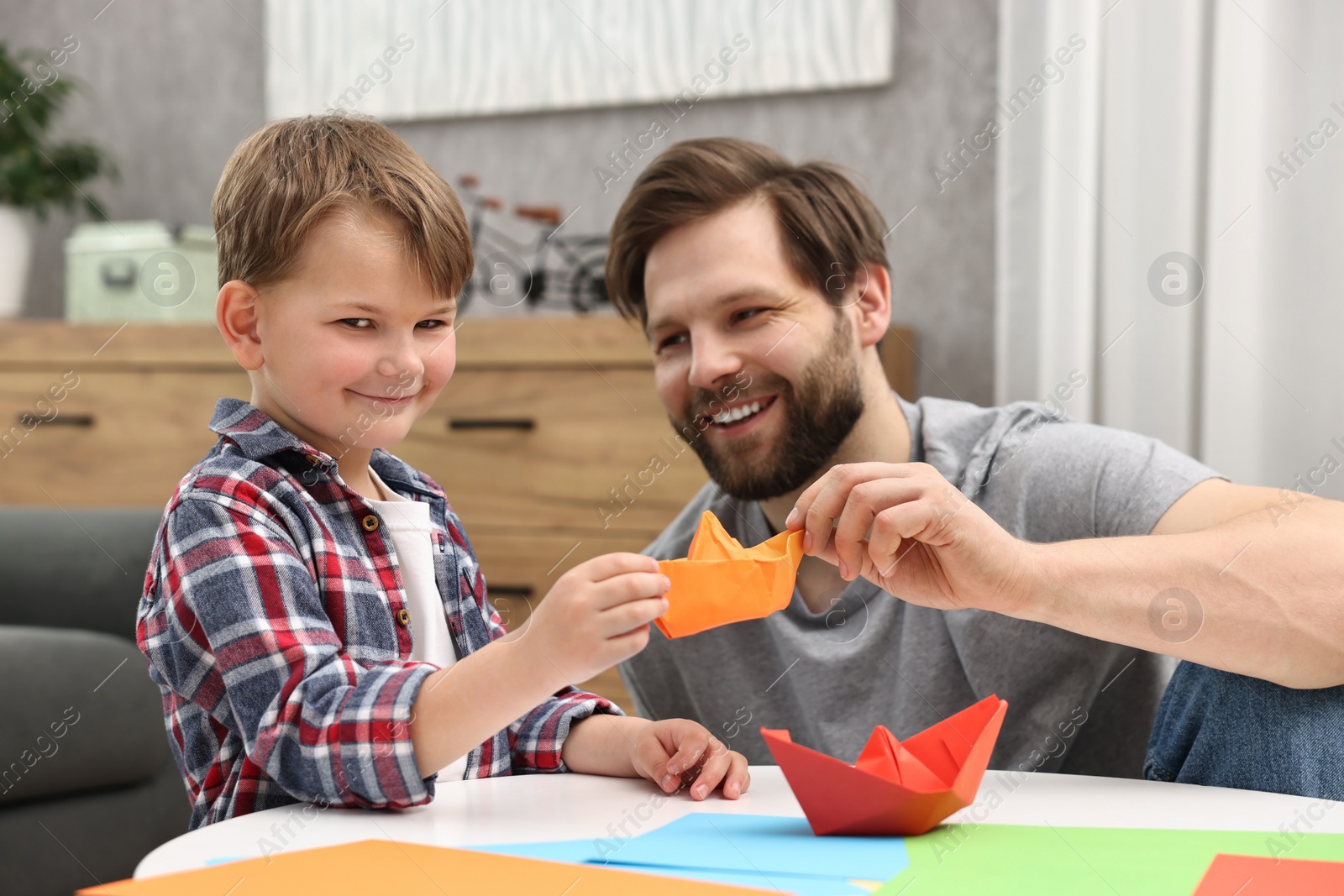 Photo of Dad and son making paper boats at coffee table indoors