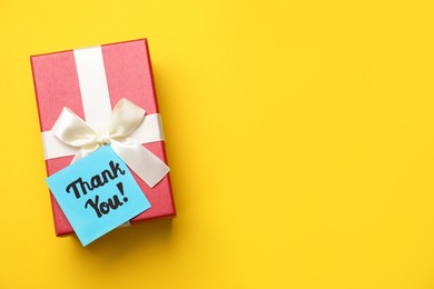 Photo of Gift box and light blue paper note with phrase Thank You on yellow background, top view. Space for text