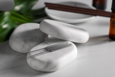 Photo of Acupuncture needles and spa stones on white table, closeup