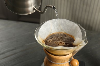 Pouring hot water into glass chemex coffeemaker with paper filter and coffee on gray table, closeup