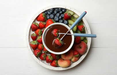 Photo of Fondue pot with chocolate and mix of fruits on white wooden table, top view
