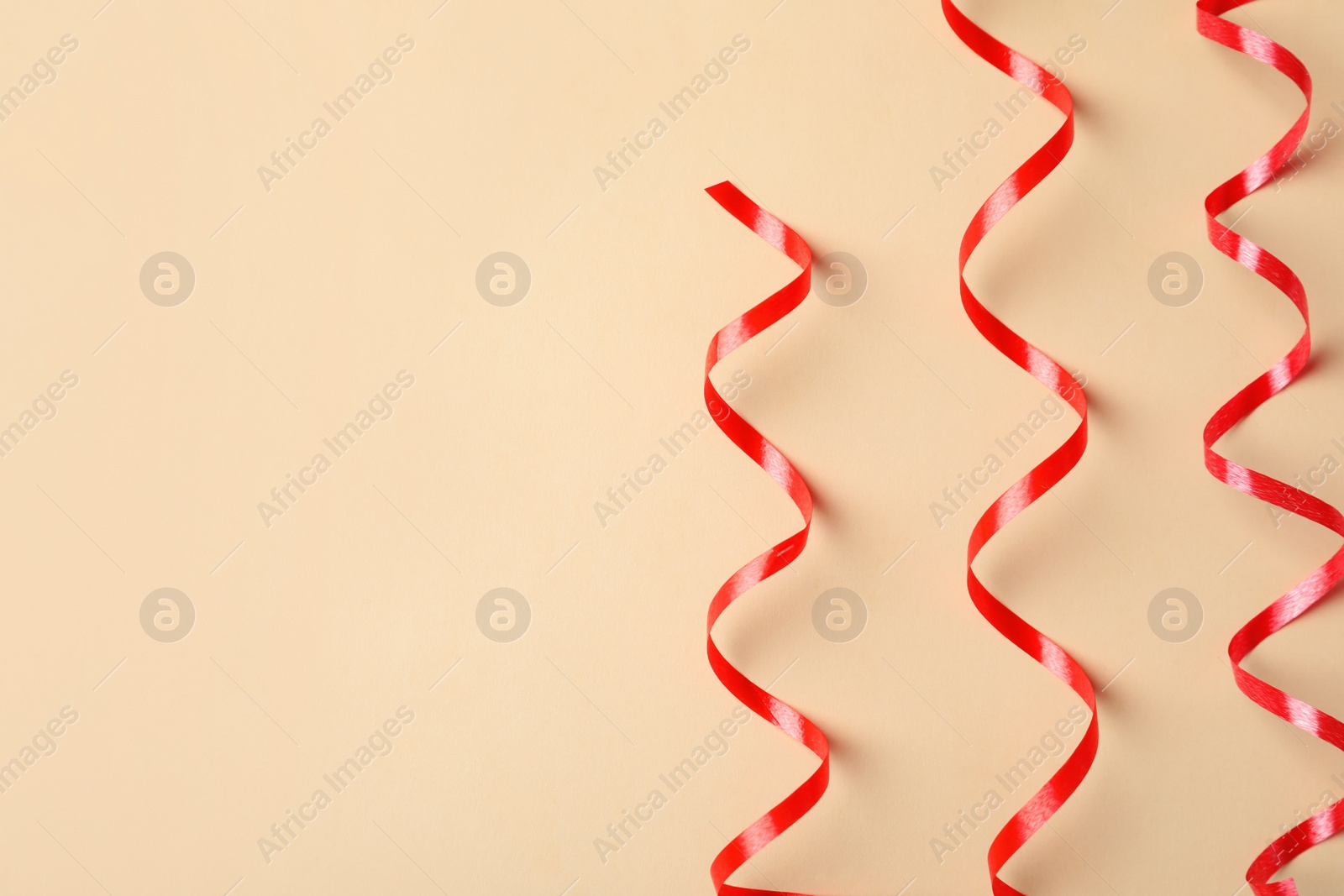 Photo of Shiny red serpentine streamers on beige background, flat lay. Space for text