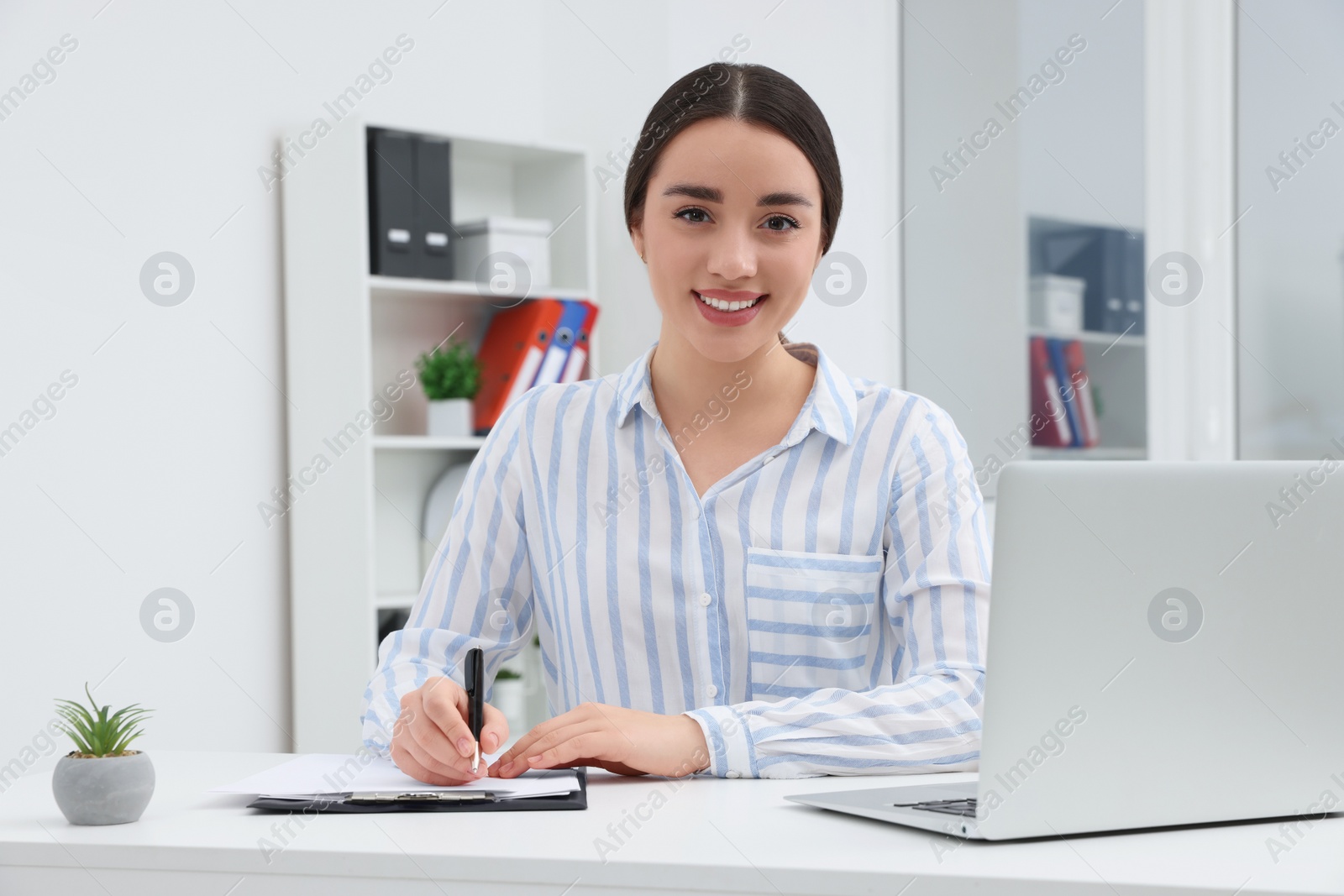 Photo of Young female intern working with laptop at table in office