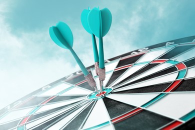 Dart board with turquoise arrows hitting target against sky