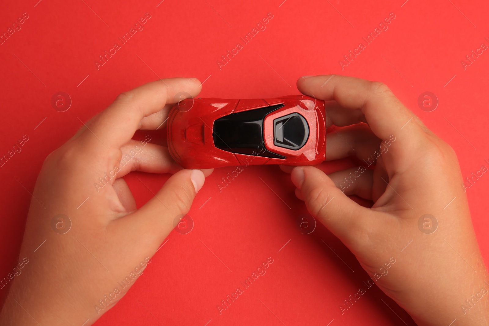 Photo of Child holding toy car on red background, top view