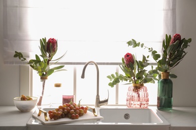 Vases with beautiful protea flowers near sink in kitchen. Interior design