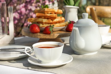 Photo of Freshly baked waffles and cup of tea on table in garden